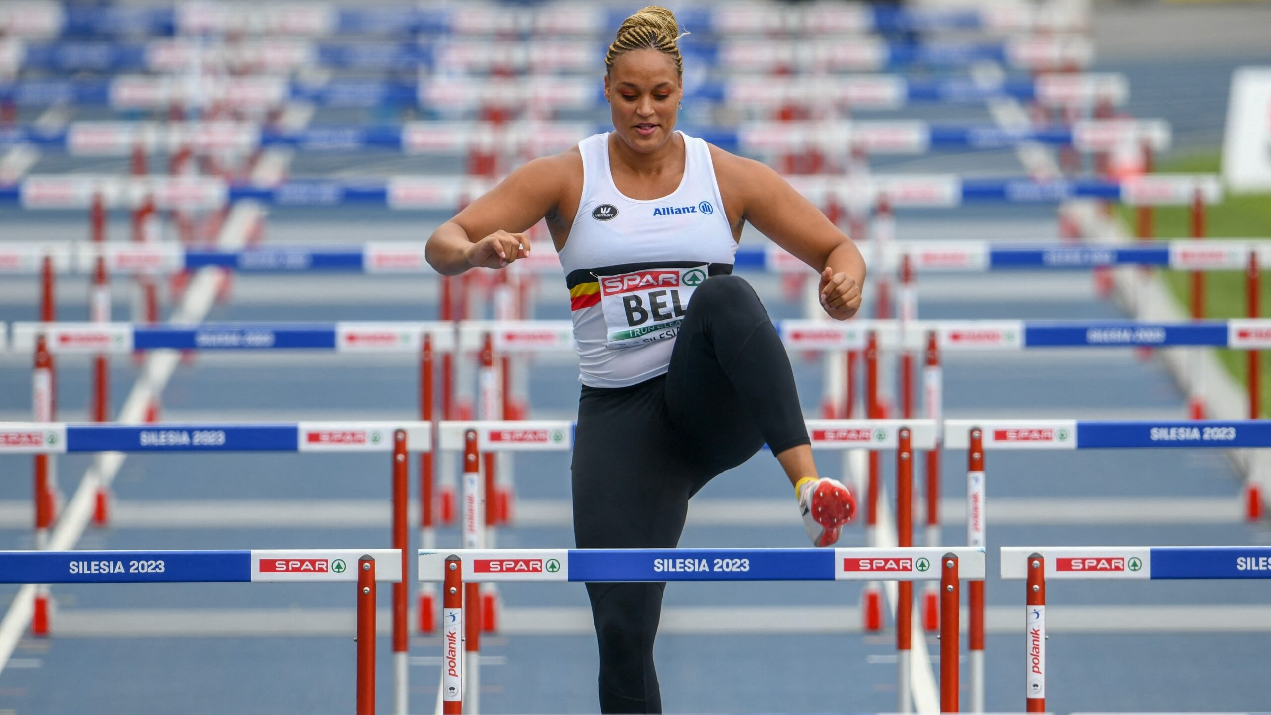 A Belgian shotputter runs the hurdles after answering her team's call