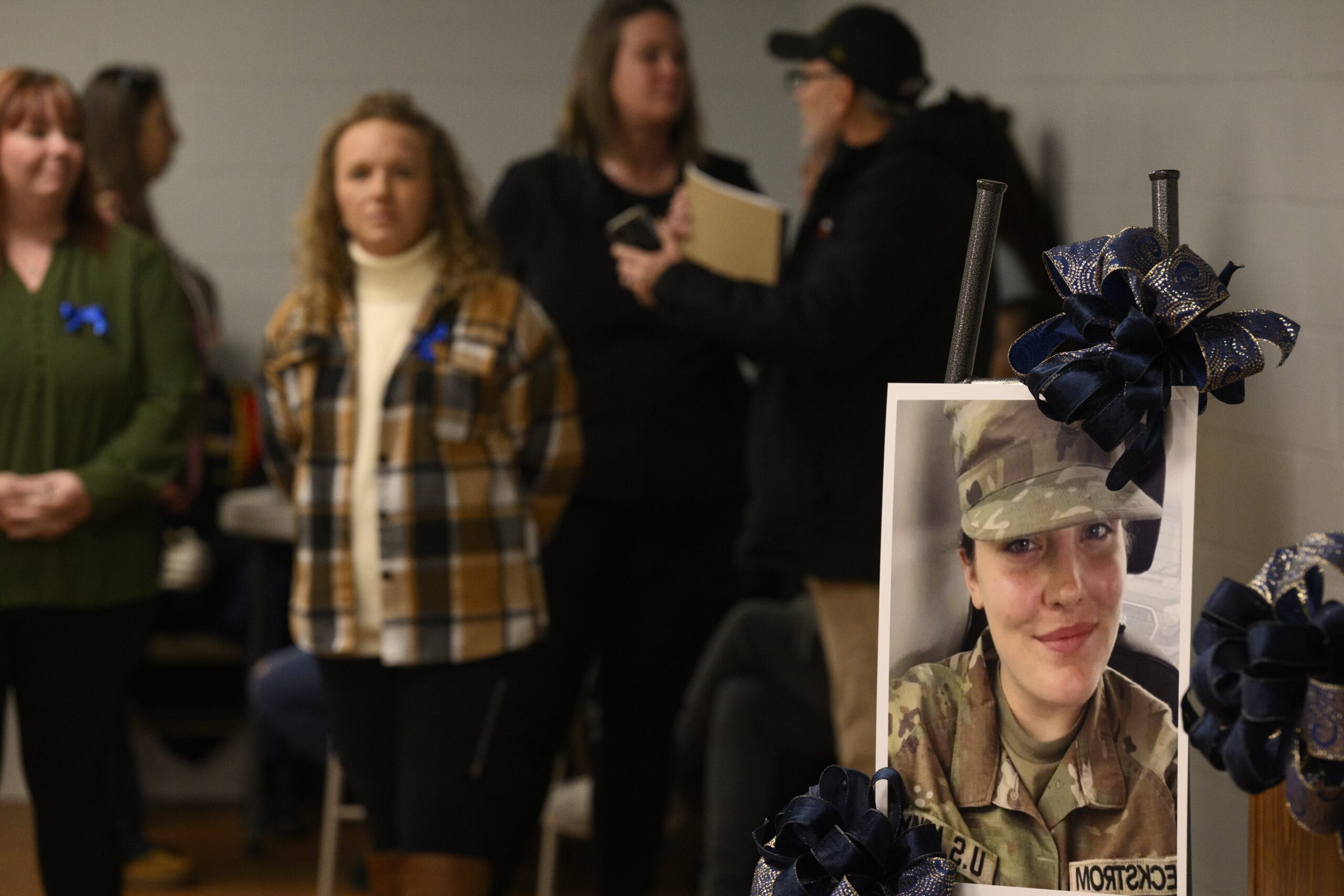 A portrait of West Virginia National Guard Specialist Sarah Beckstrom, in uniform, sits on an easel with a black bow on it as community members gather in the background.